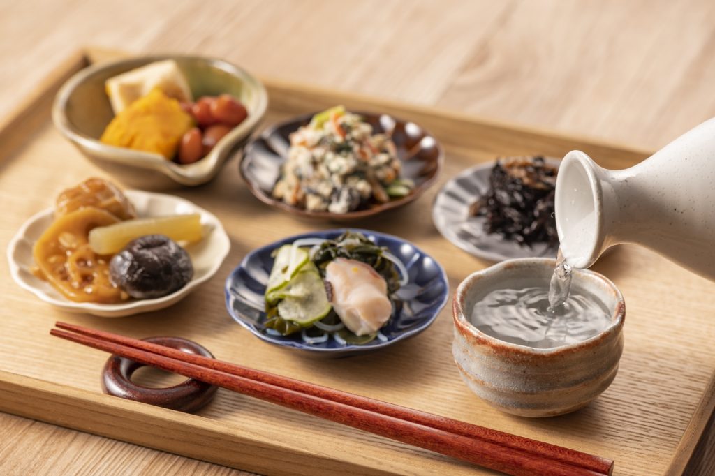 Japanische Otsumami mit mehreren kleinen Gerichten und Sake auf dem Tisch